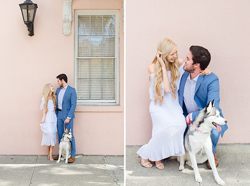 engaged couple poses with husky along pink house on Rainbow Row