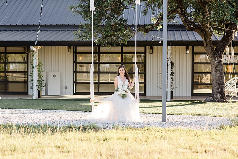 bride sits on swing outside Mae's Ridge barn