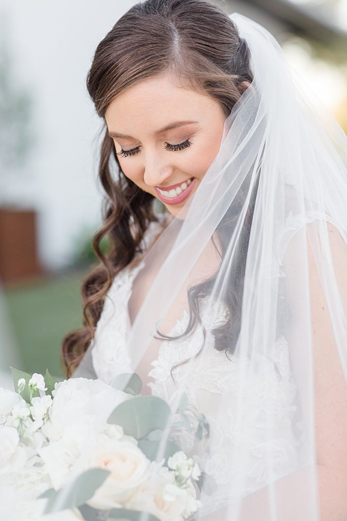 bride smiles at bouquet while veil is draped over her shoulder