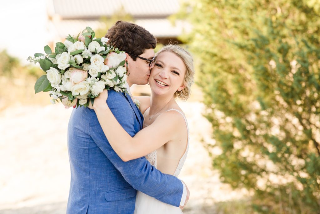groom kisses bride on the cheek while she holds bouquet behind his head