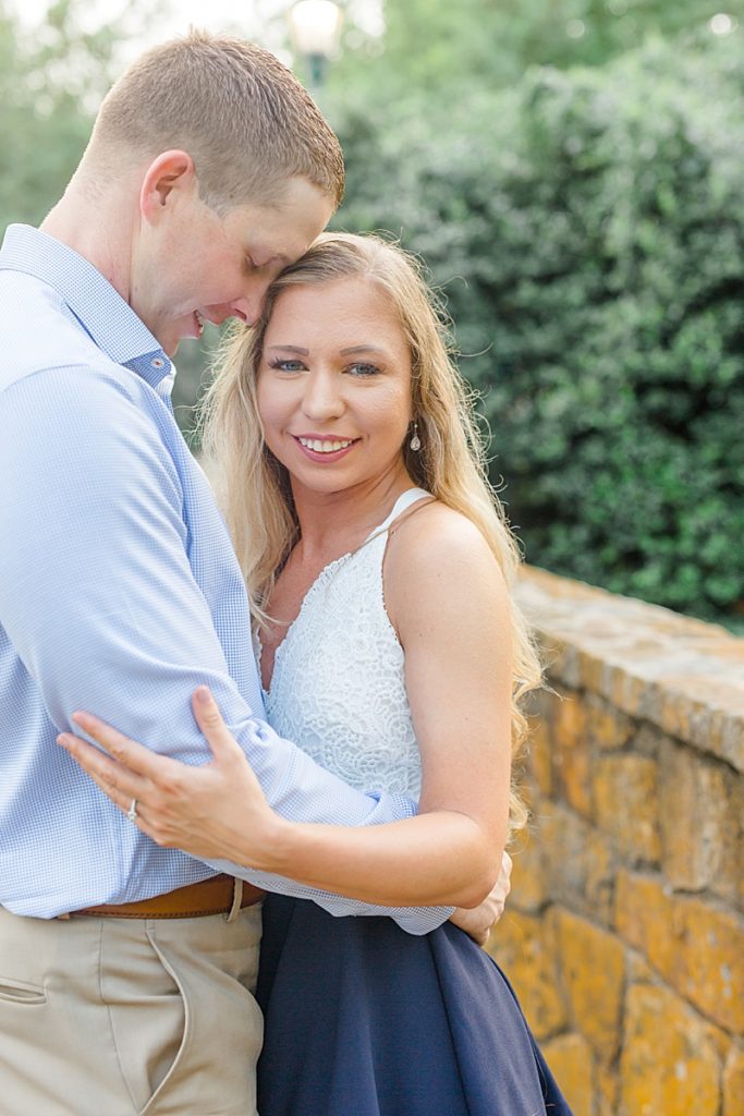 bride to be smiles at photographer while groom hugs her