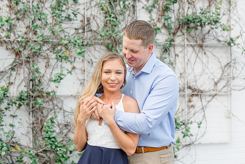 engaged couple embraces by ivy covered wall