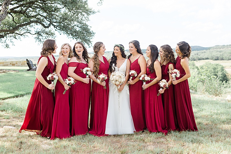 bride and bridesmaids in red gowns pose overlooking hills of Austin TX