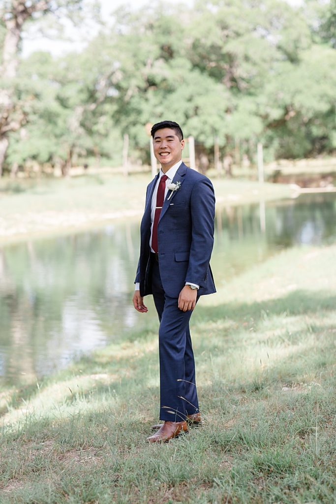 groom poses by lake on Austin Texas ranch
