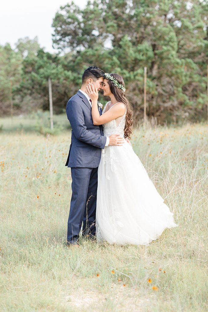 bride holds groom's face during portraits in field