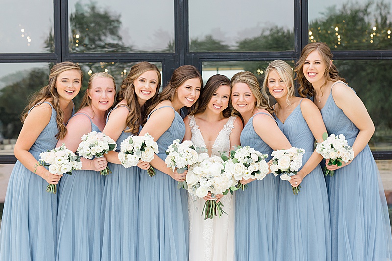 bridesmaids in blue gowns with white bouquets smile with bride