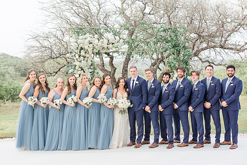 bride and groom pose with bridal party in blue gowns and blue suits