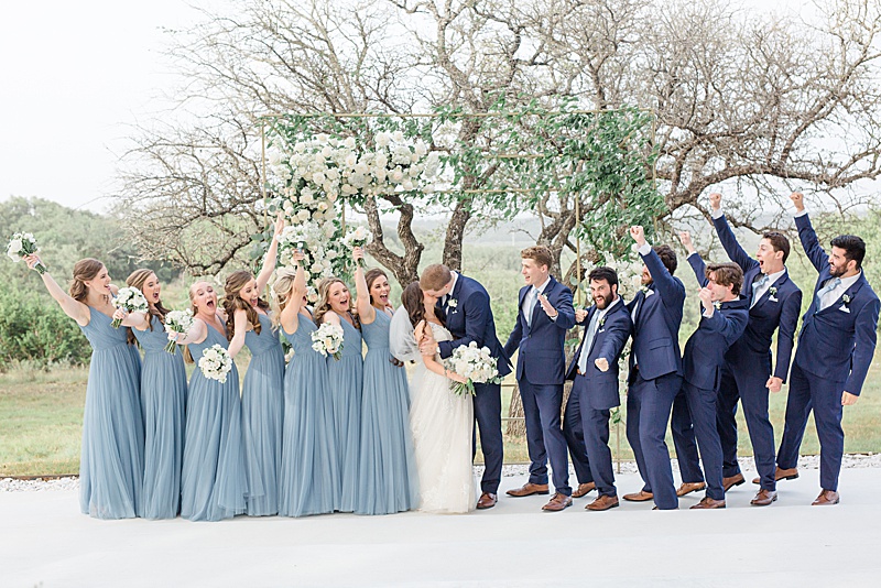 bridal party cheers while bride and groom kiss