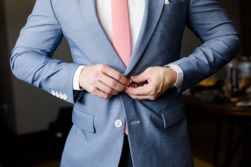 groom adjusts navy suit with pink tie