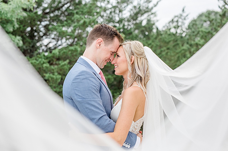 bride and groom touch noses while veil flows around them
