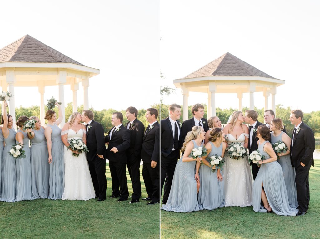 bridal party in blue gowns and black tuxes cheer by gazebo as bride and groom kiss