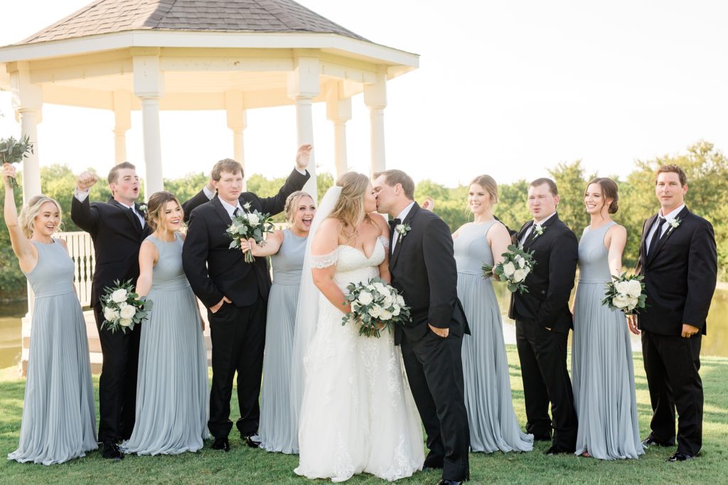 bride and groom kiss while wedding party surrounds them at The Milestone Denton