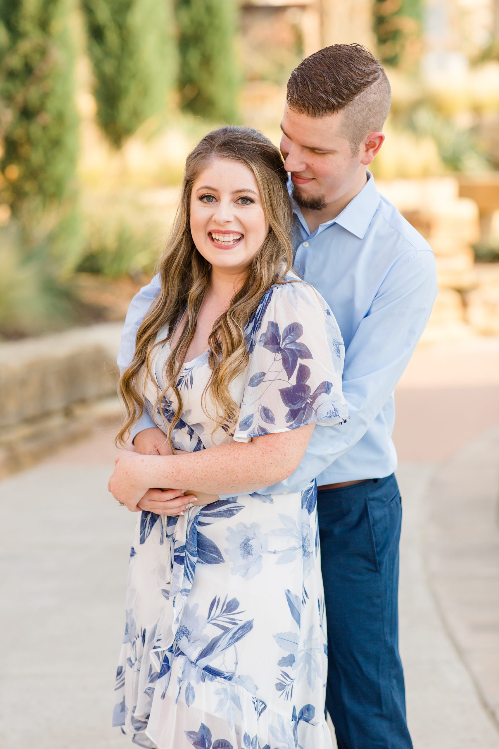 groom hugs bride from behind during Dallas Arboretum engagement session