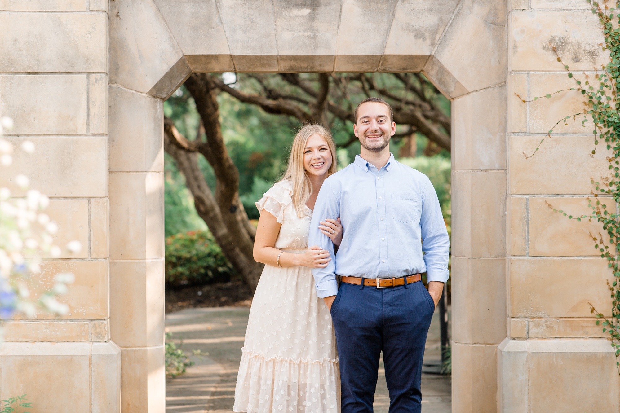 bride and groom pose by stone archway during engagement session