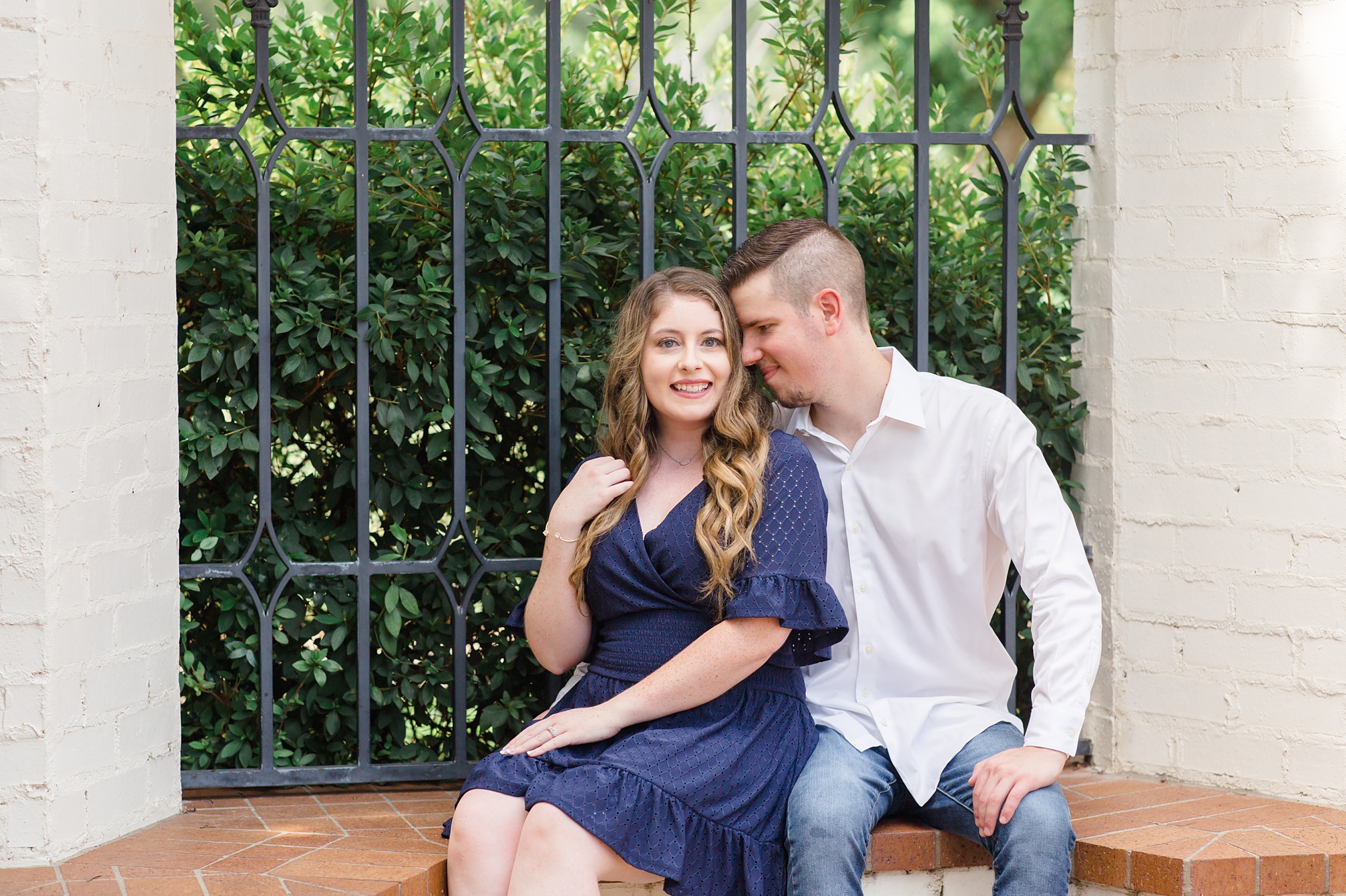 engaged couple sits by wrought iron gate at Dallas Arboretum