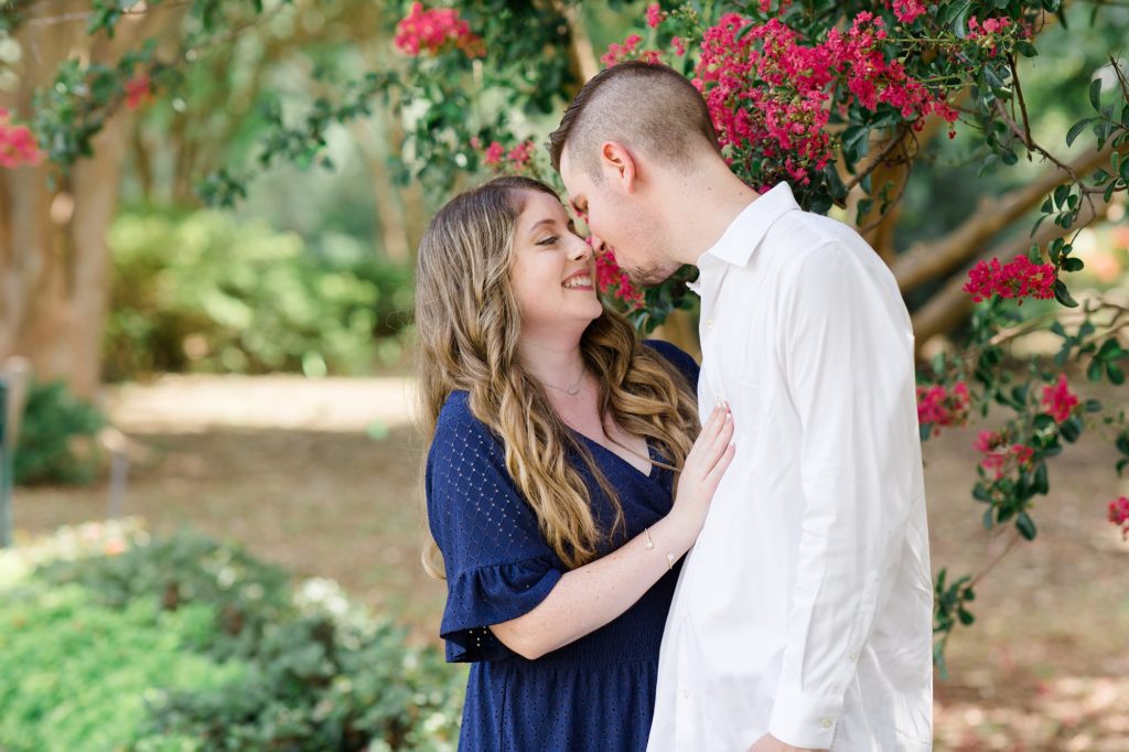 couple poses by pink bush during engagement photos