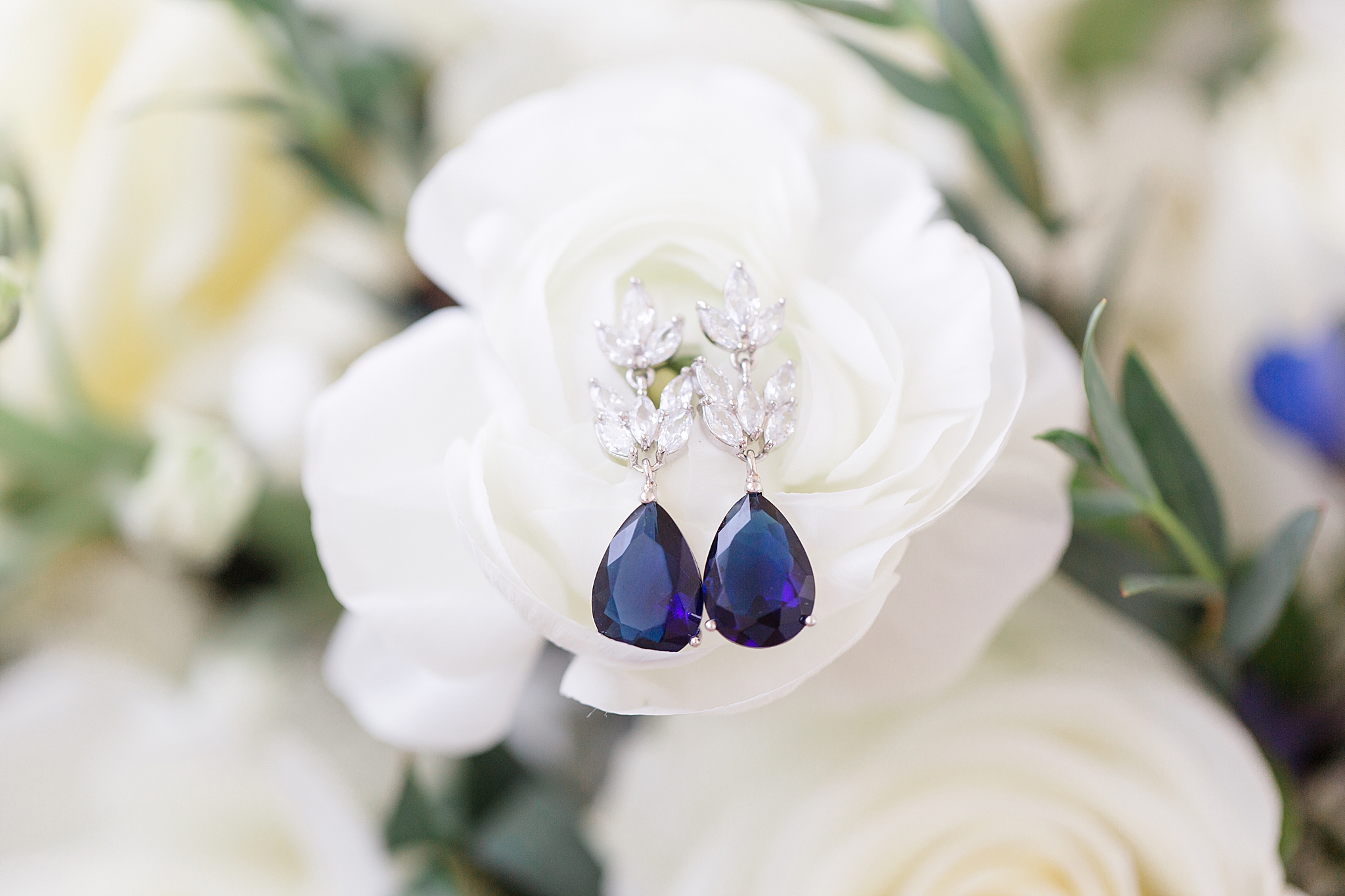 bride's blue jewel earrings rest on white flower