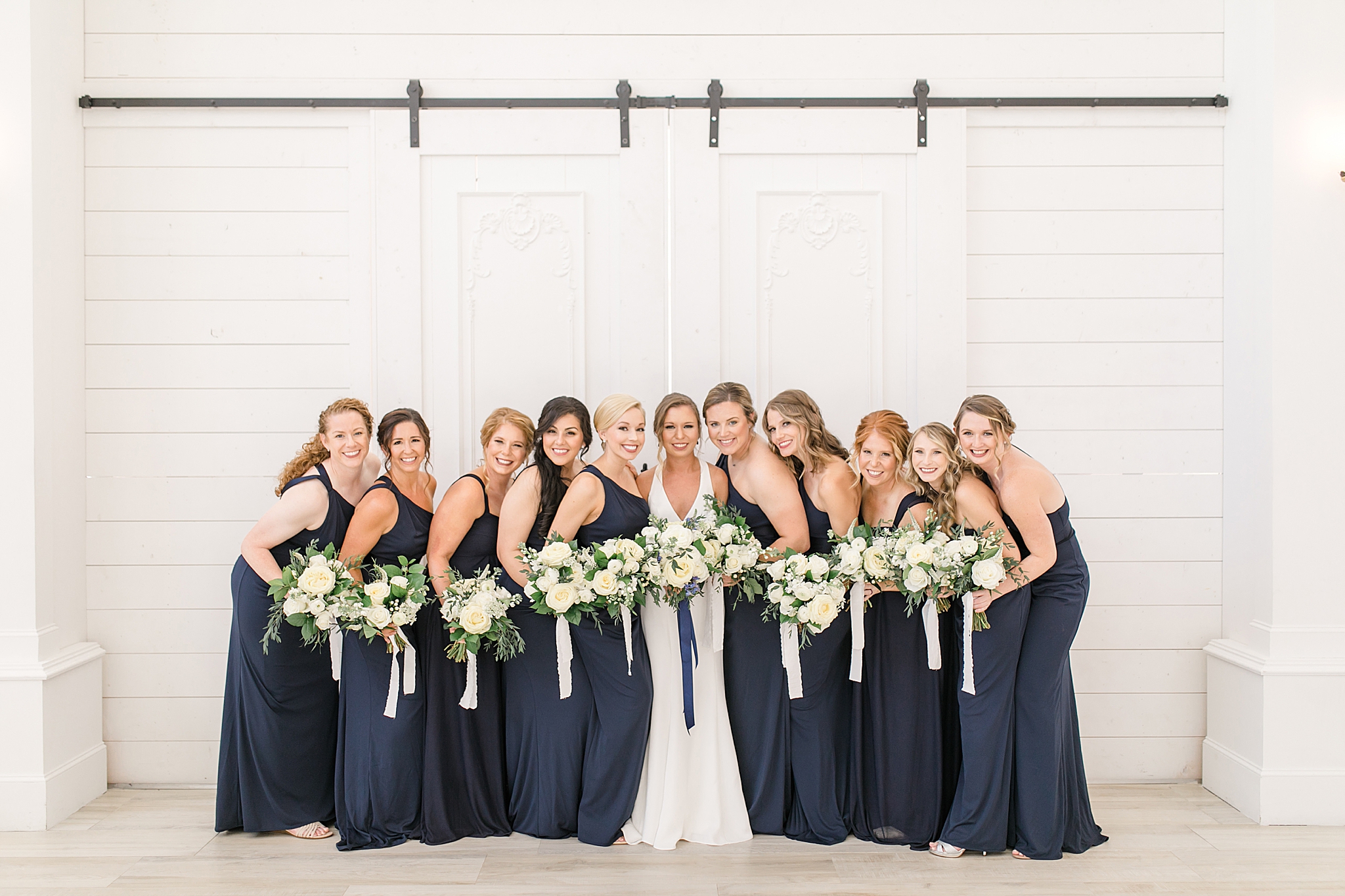 bridesmaids in navy blue gowns hold bouquets of ivory flowers with navy ribbons