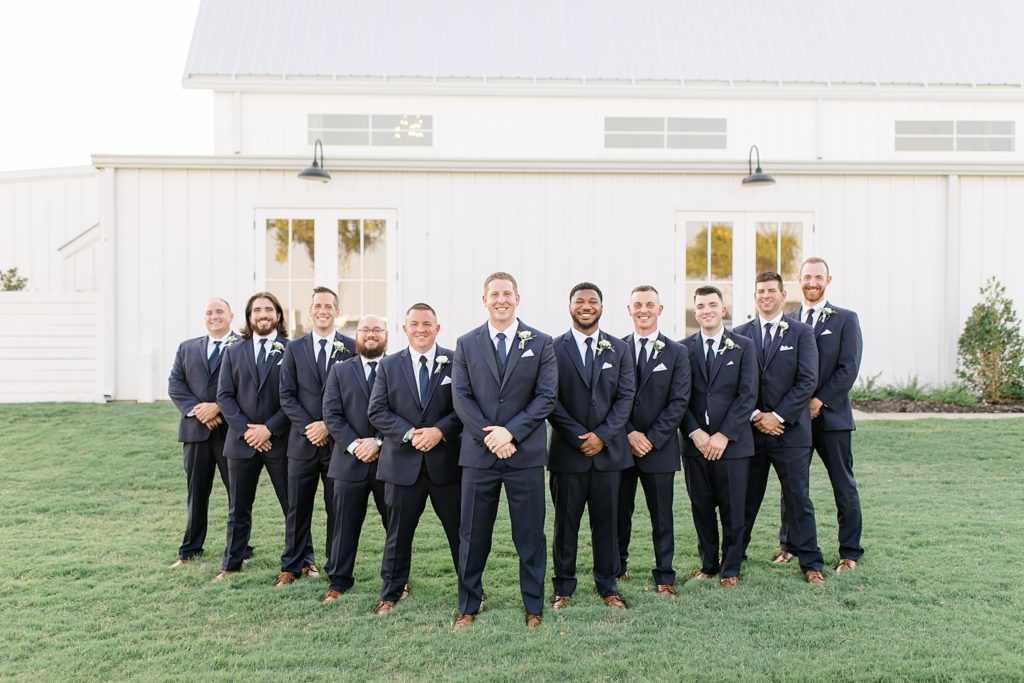 groom poses with groomsmen outside The Nest at Ruth Farms