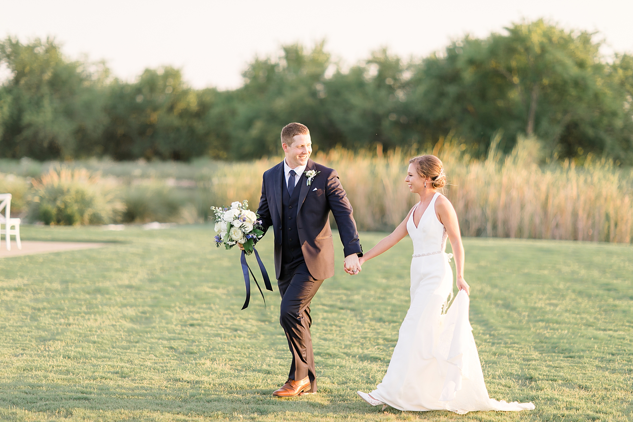 groom leads bride through field at The Nest at Ruth Farms