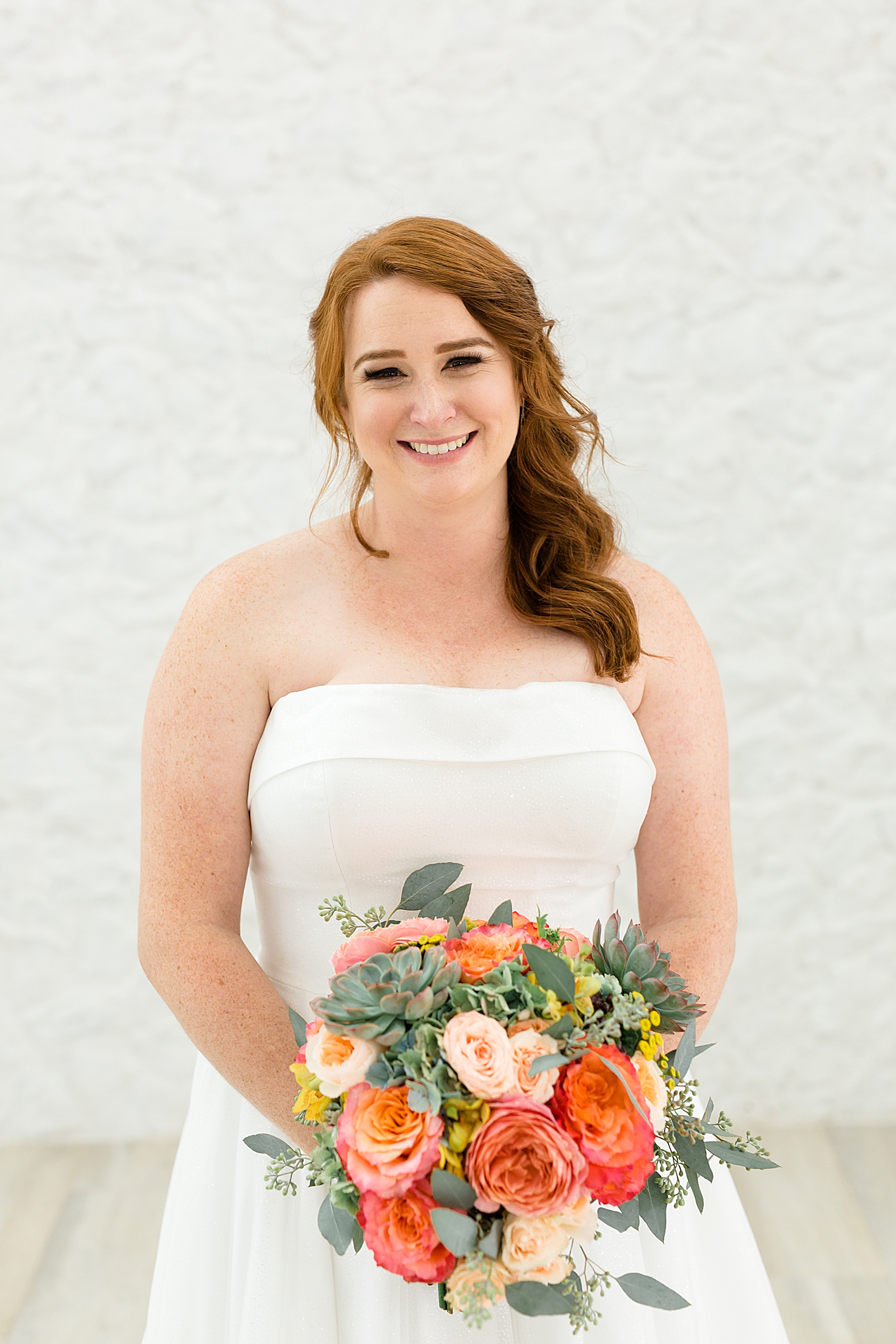 bride in strapless gown holds bouquet of bright flowers and succulents