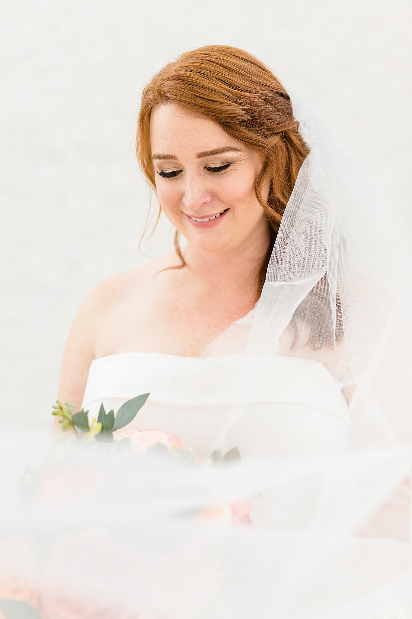 bride with veil around shoulders looks at flowers