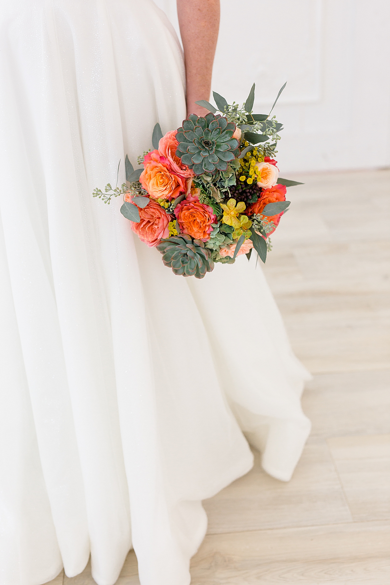 bride holds bouquet of succulents and bright flowers to the side