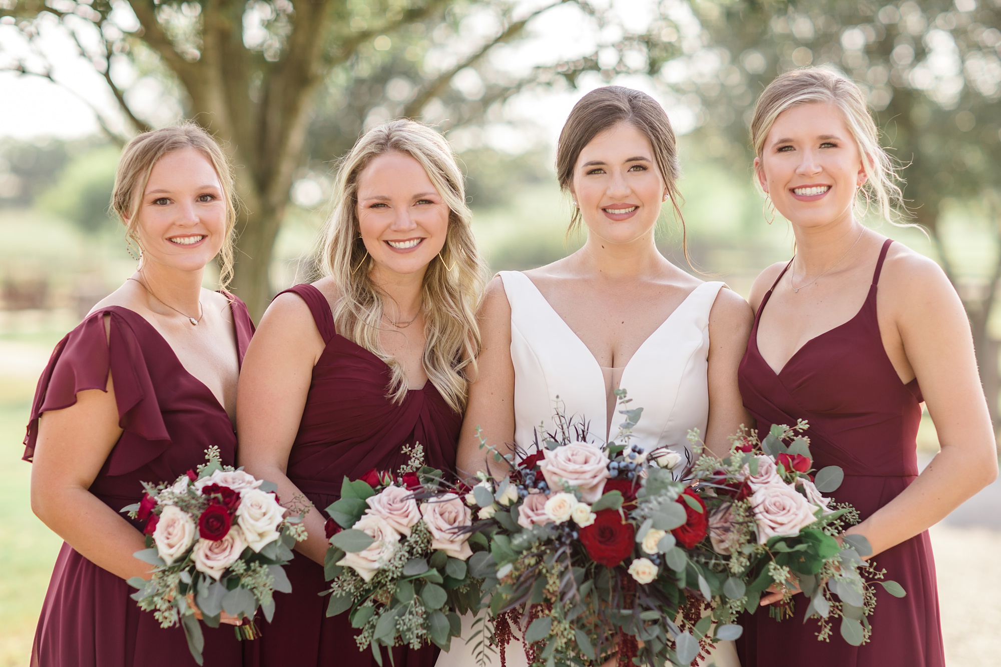 bride poses with bridesmaids in cranberry gowns