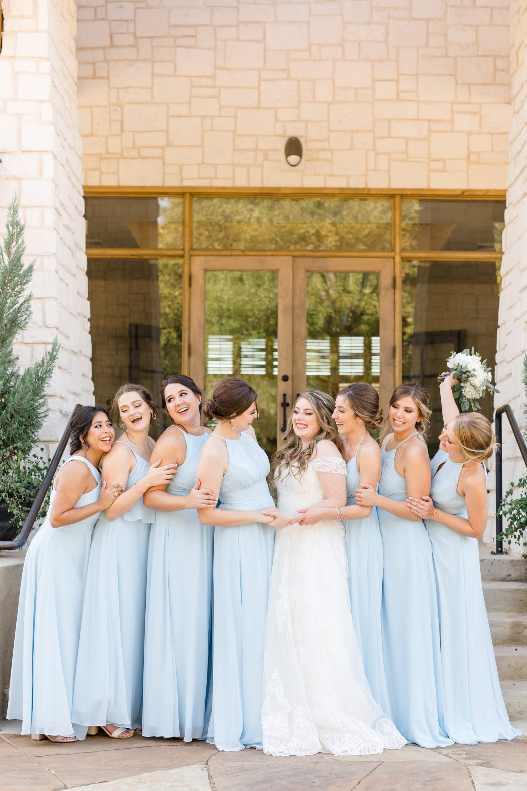 bridesmaids in light blue gowns stand with bride outside Hidden Pines Highland Village