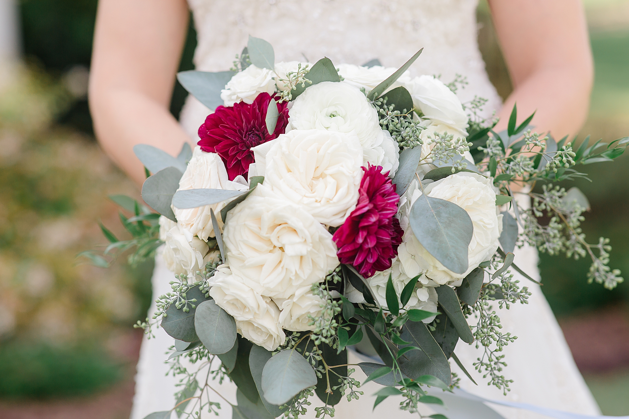 bride holds bouquet of ivory and red flowers