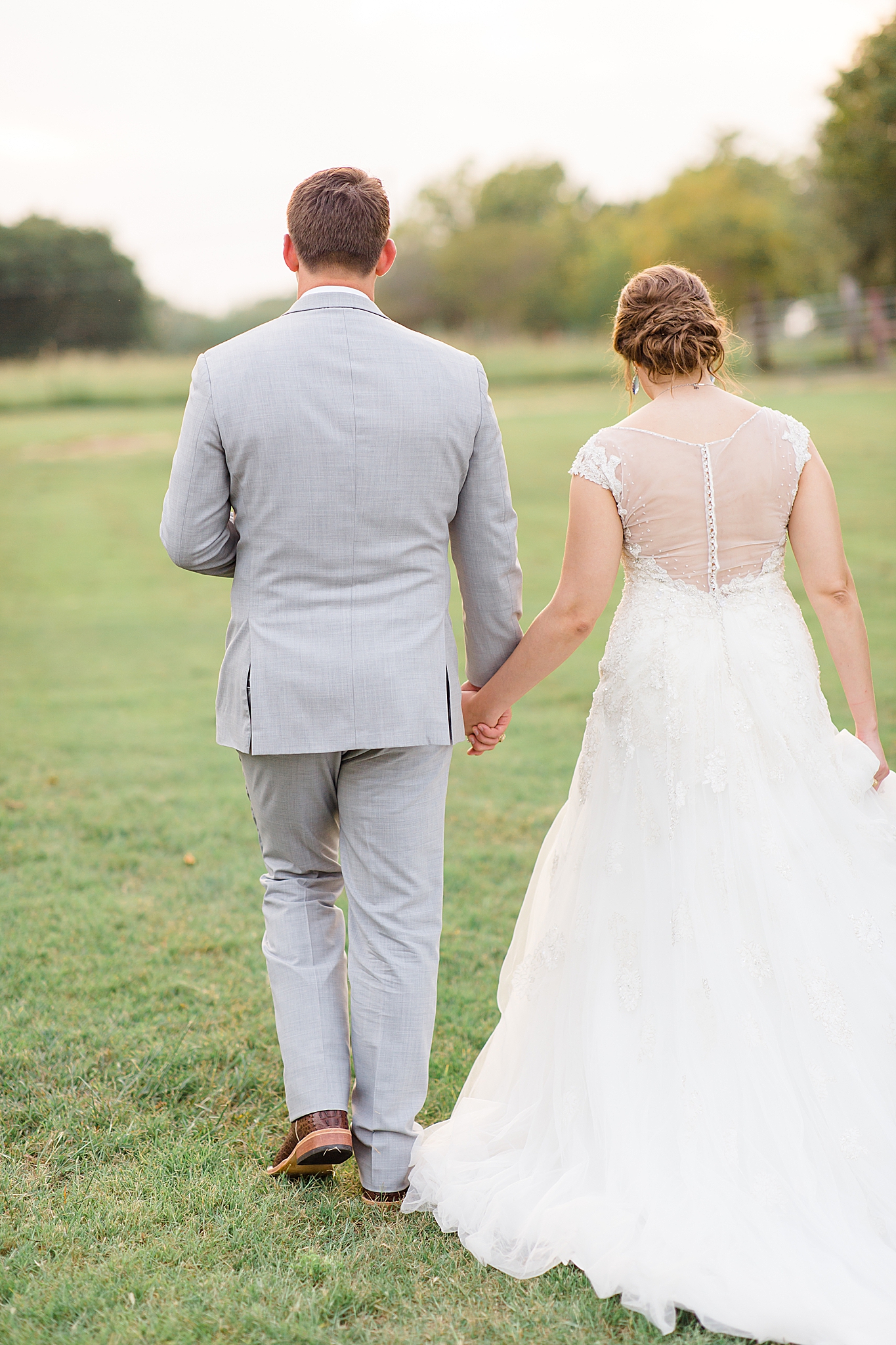 groom holds bride's hand and walks along Rustic Grace Estate