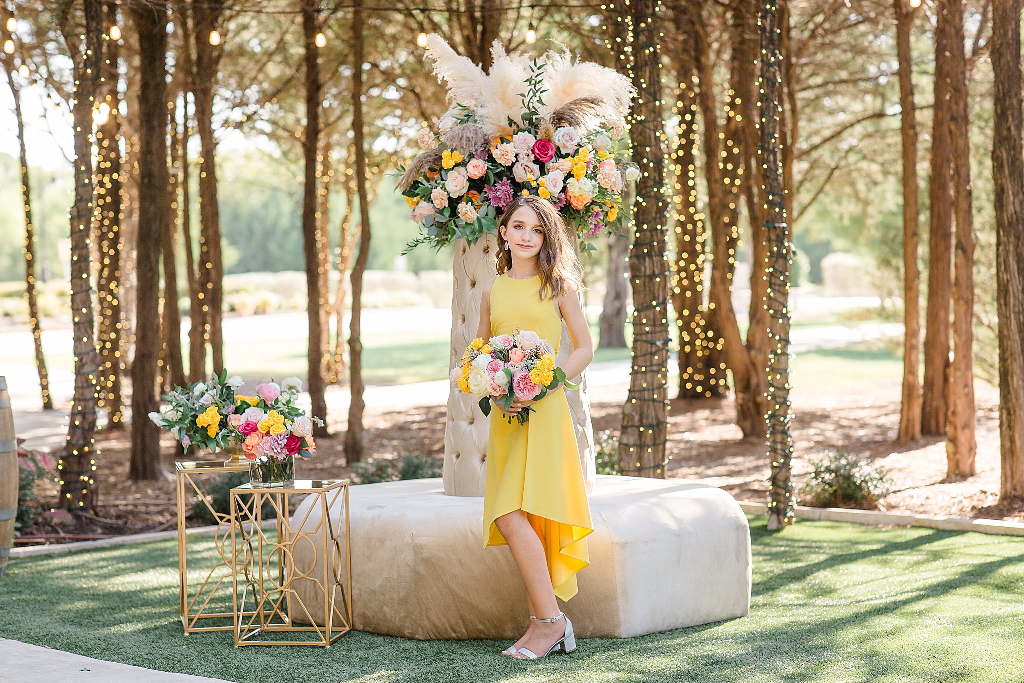 bridesmaid in yellow gown poses by floral display in Texas