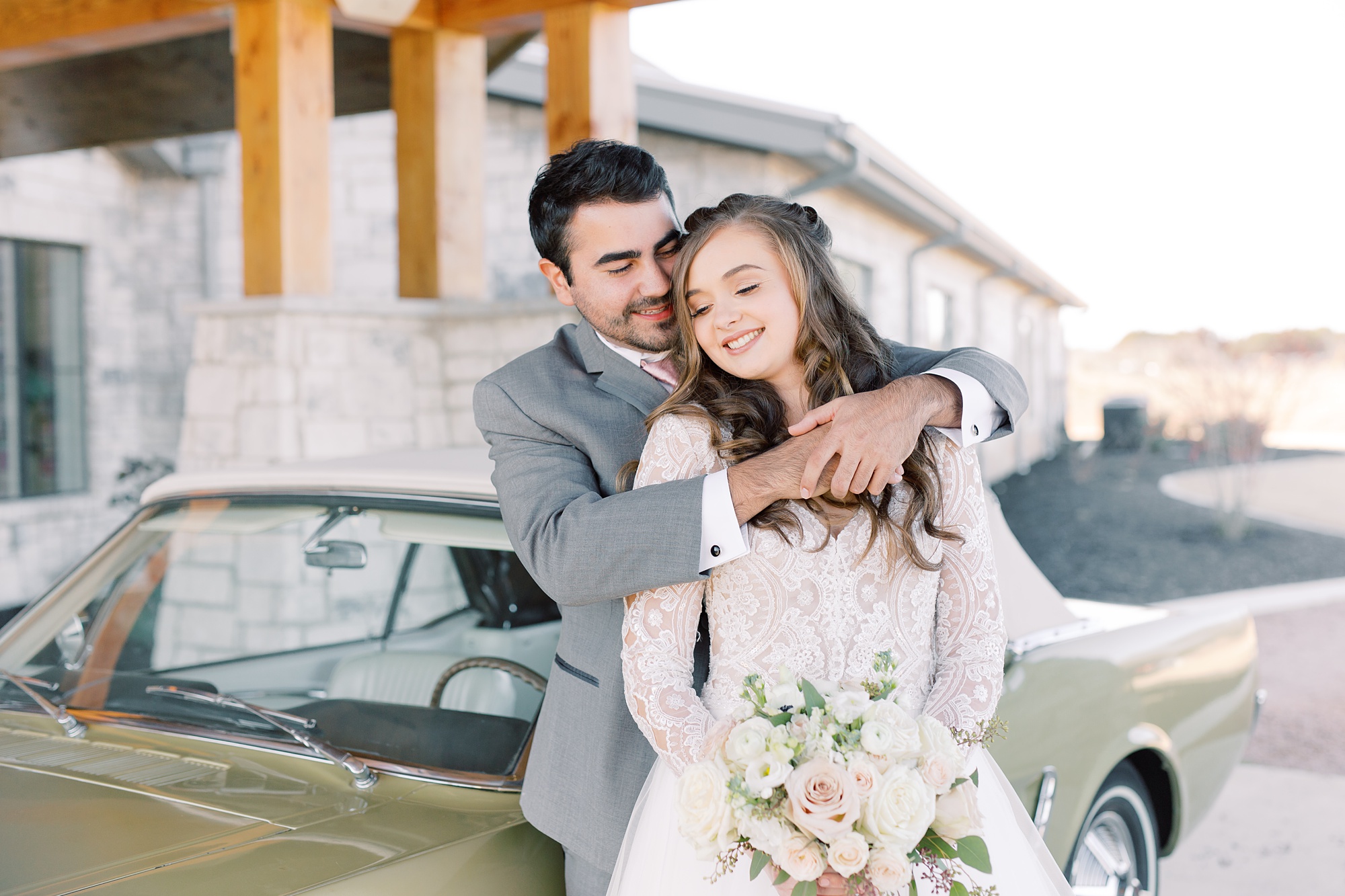 groom hugs bride by vintage getaway car