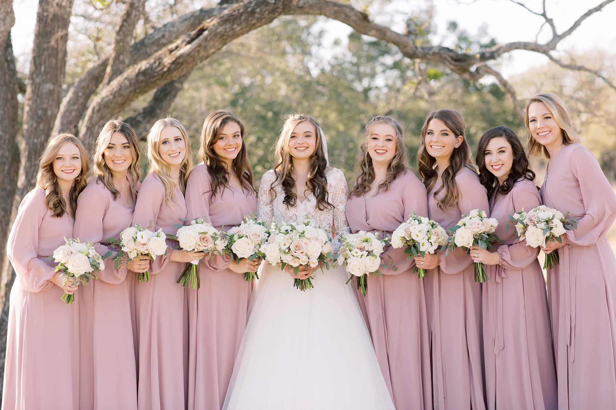 bride poses with bridesmaids in pale pink gowns