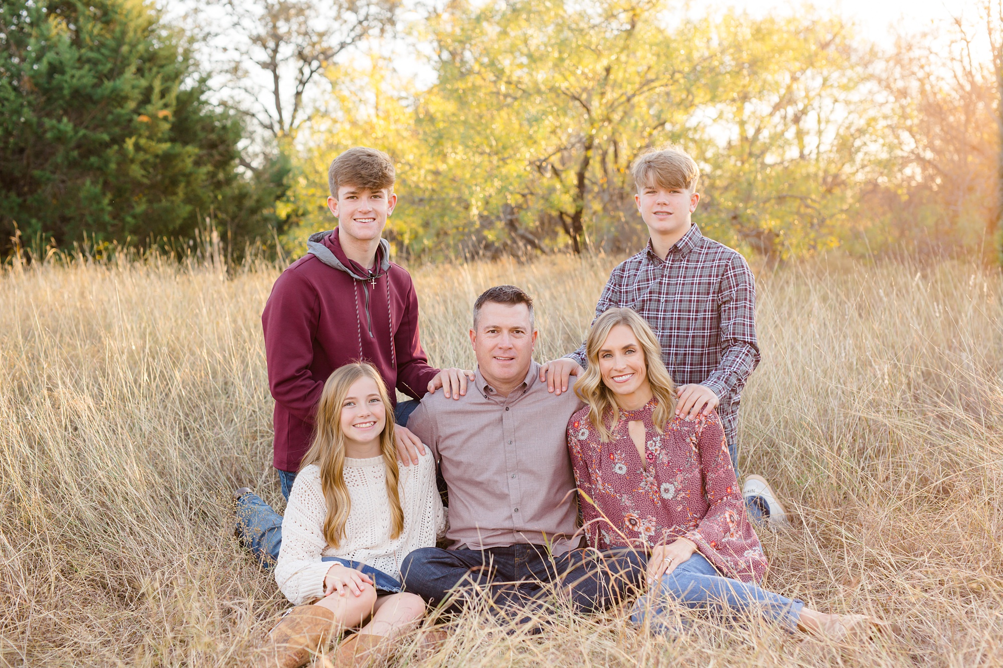 parents sit with three kids in field during Texas family photos