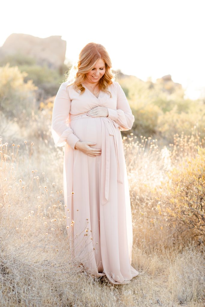 mom looks down at belly during maternity portraits in the desert