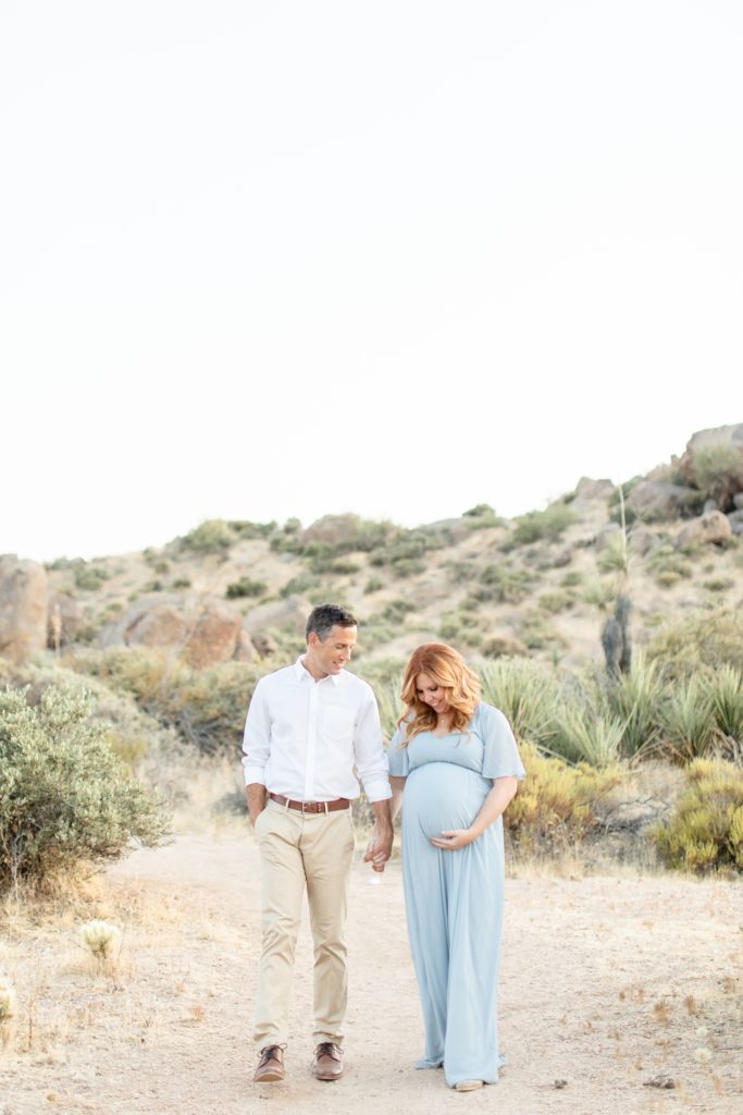 husband and wife walk through AZ desert during maternity photos