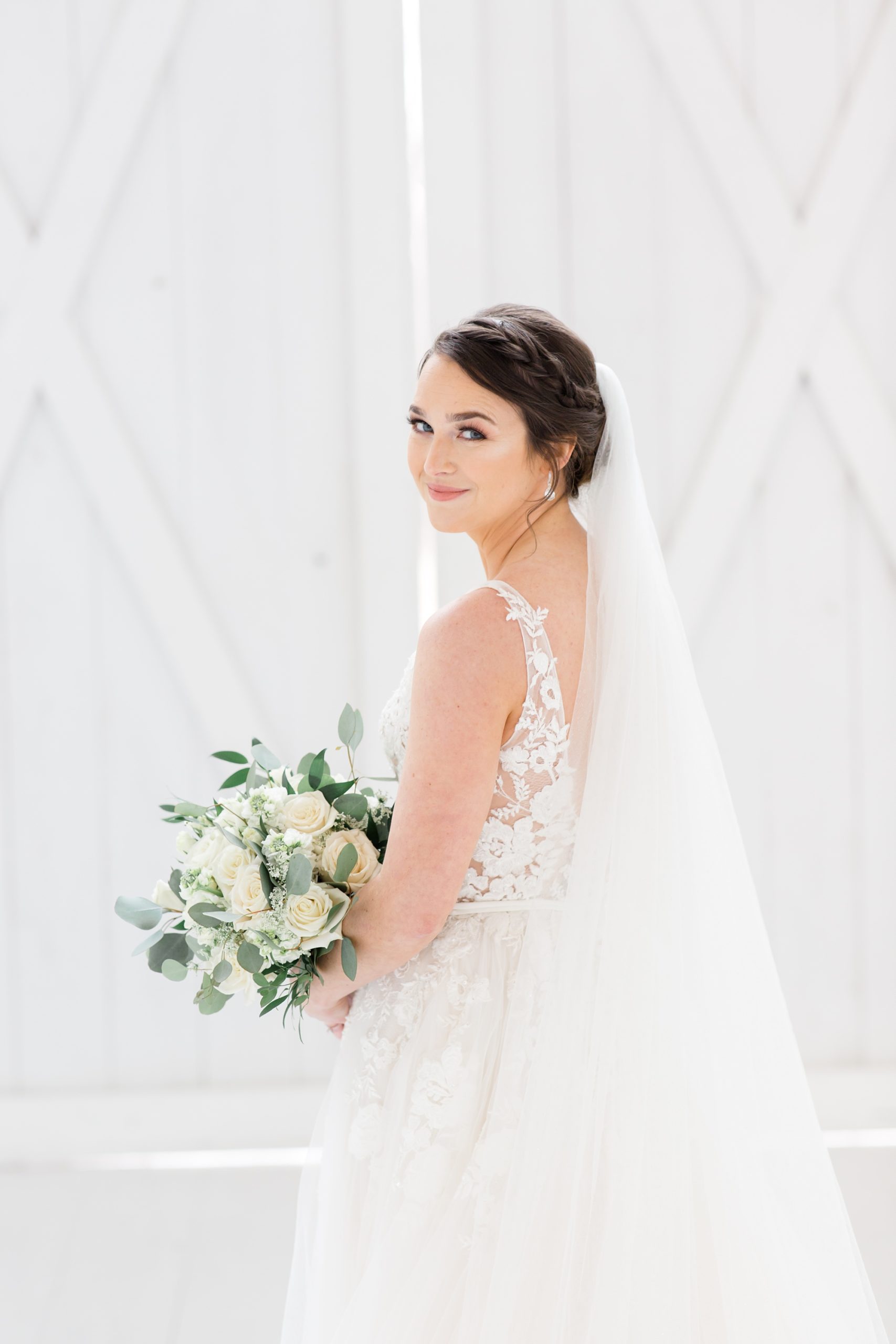 bride holds bouquet with veil wrapped around shoulders