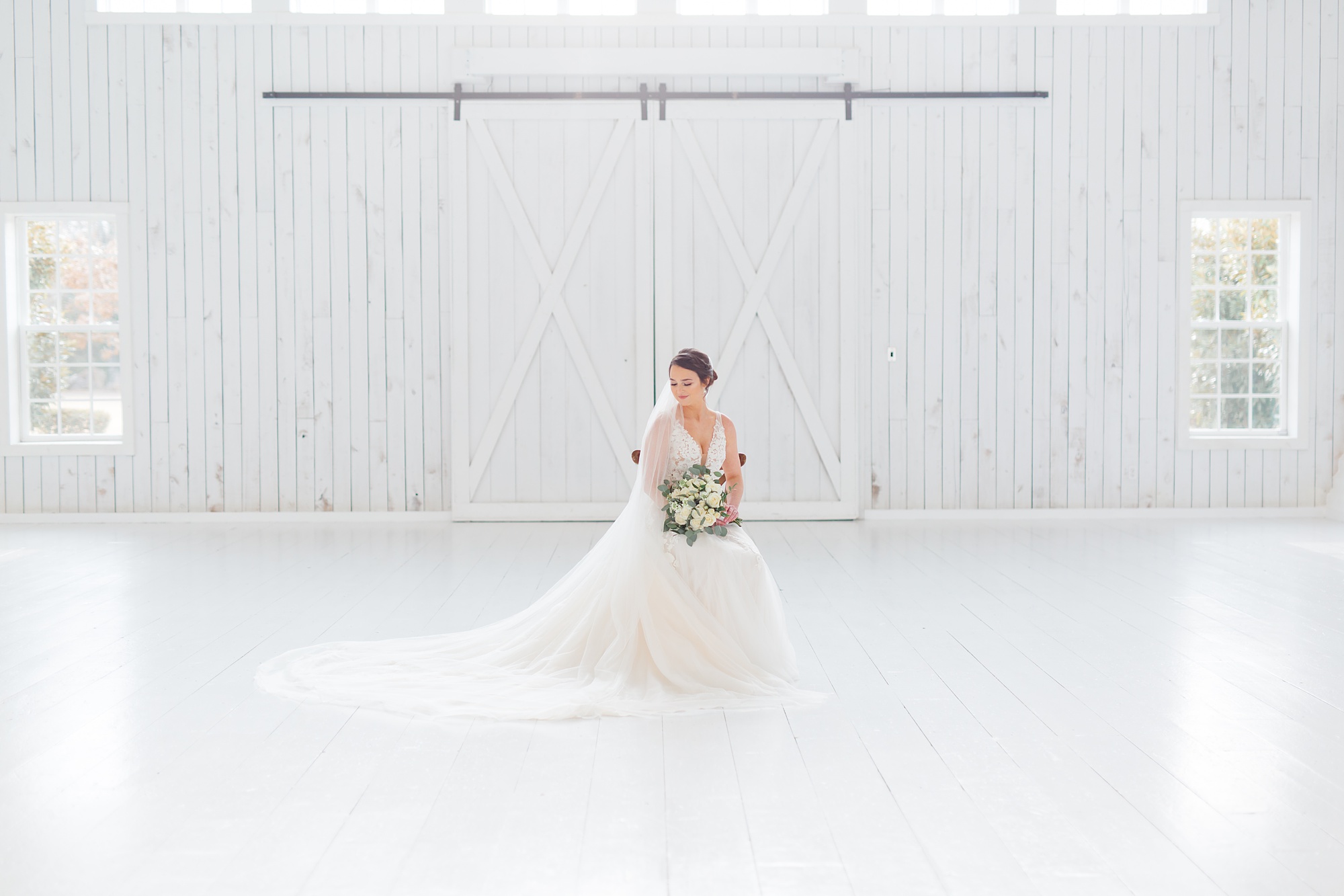 bride sits in wooden chair with cathedral veil spread on floor