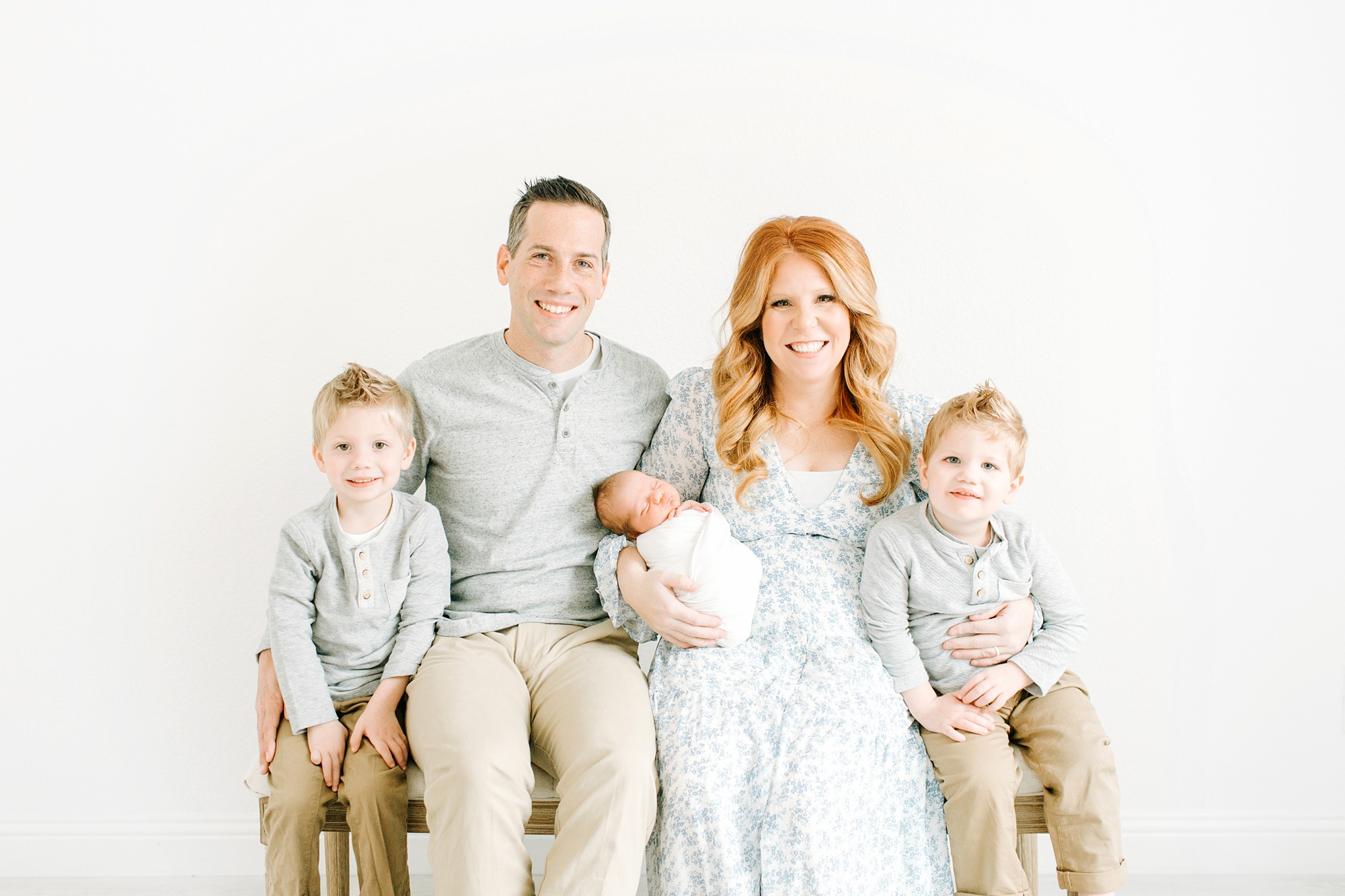 family of five sits on bench during studio newborn photos in Texas