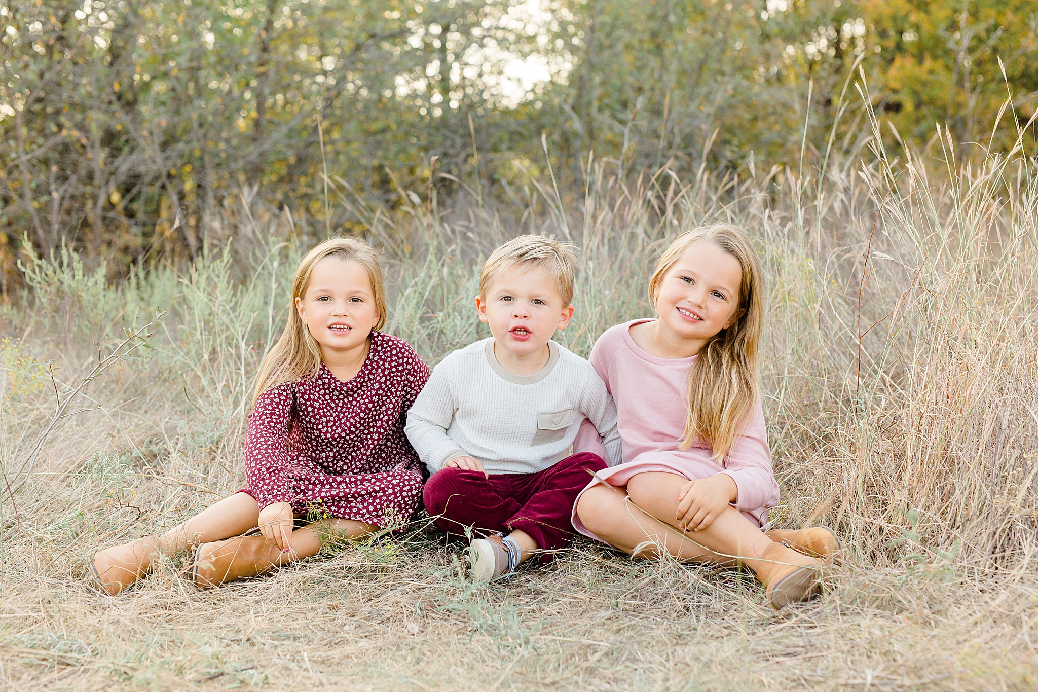 three siblings sit in tall grass at Murrell Park