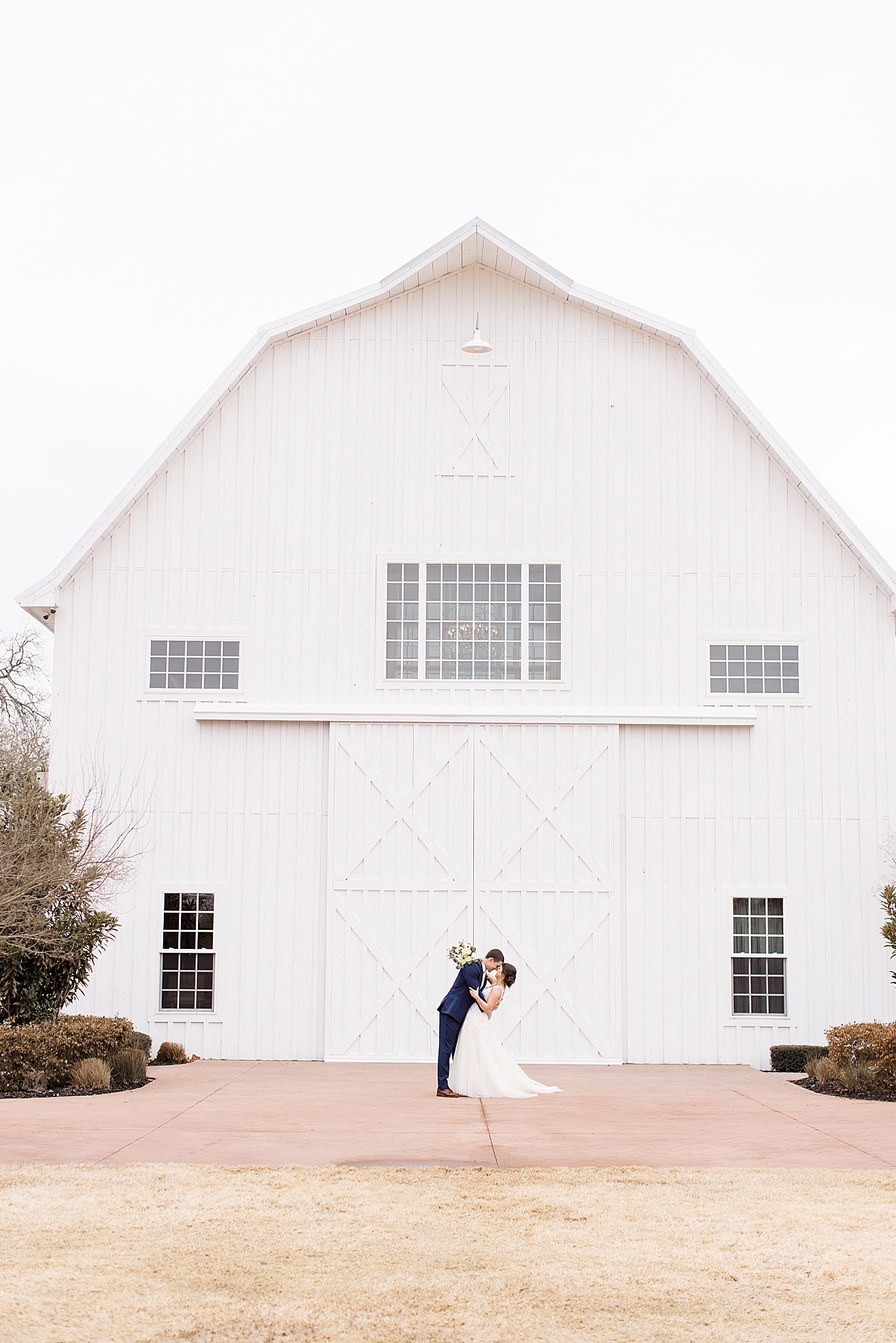 couple kisses in front of white barn in Dallas TX