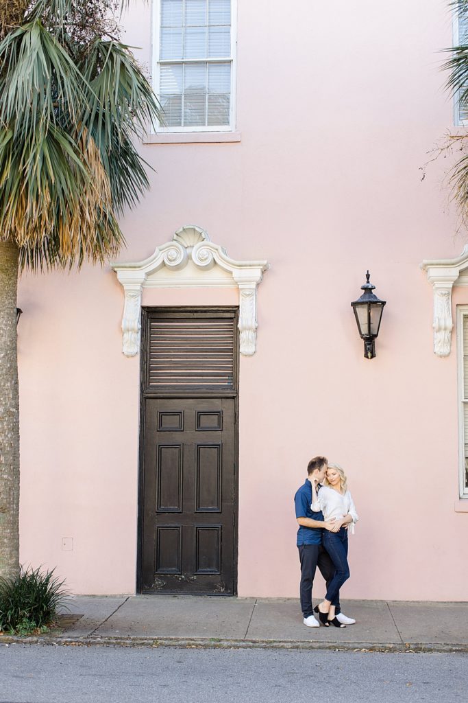 married couple hugs by pink house during Charleston anniversary portraits
