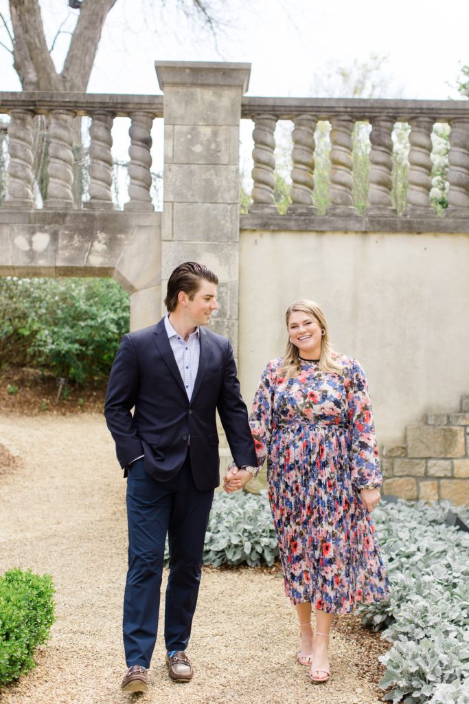 groom holds fiancees hand during Dallas Arboretum engagement photos