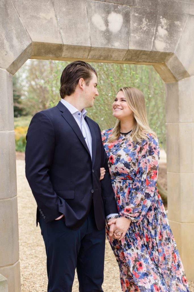 couple poses under stone bridge in Dallas Arboretum