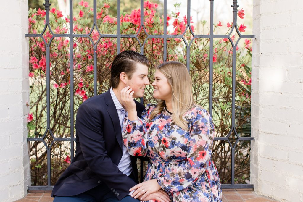 bride holds groom's chin during Dallas Arboretum engagement photos