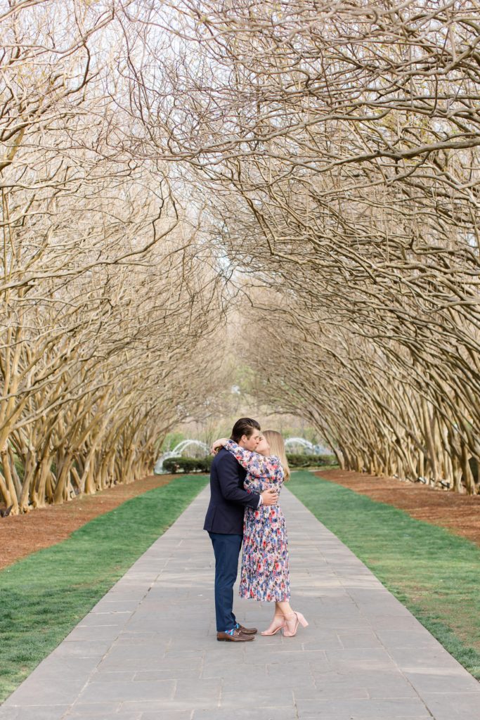 bride and groom kiss on covered walkway during Dallas Arboretum engagement photos 