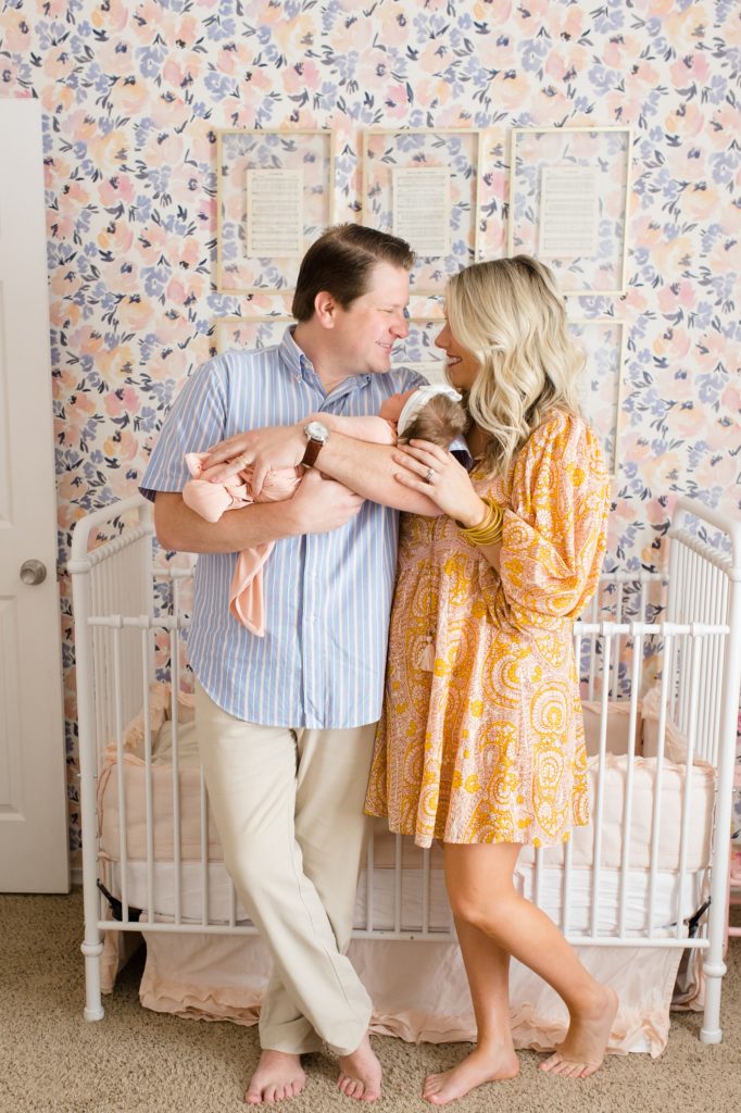 parents laugh together by crib during Dallas lifestyle newborn portraits