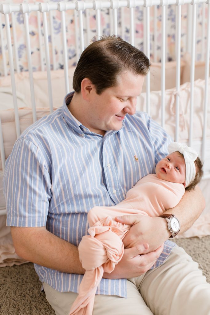 dad looks down at baby girl with white bow