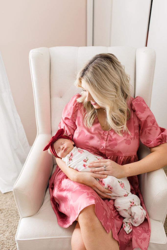 mom in pink dress holds baby girl in nursery at home 